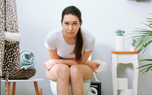 Frau sitzt gebückt auf einer Toilette